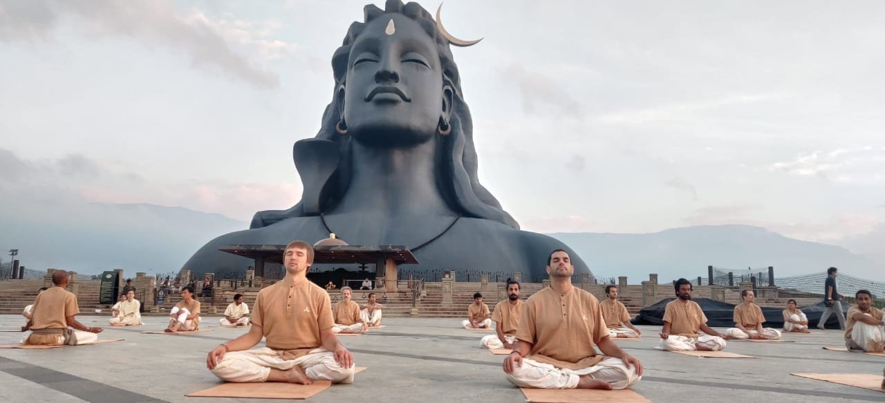 The 34-metre Adiyogi statue at the Isha Yoga Center with practitioners in cross-legged seated practice in the foreground.